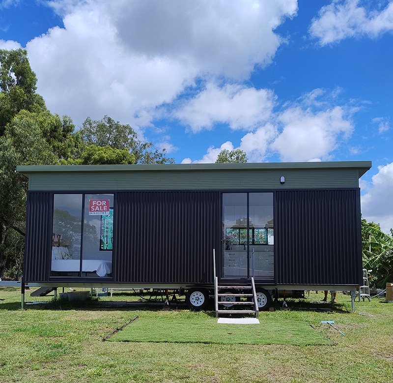 A black Big Coast tiny home on a registered trailer on a grassy Gold Coast block under a blue sky